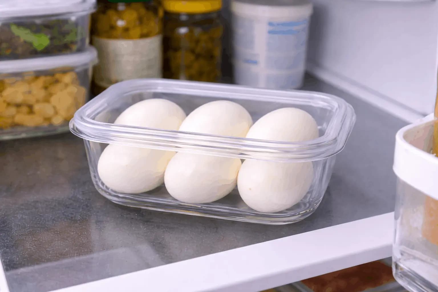 Hard-boiled eggs stored in clear container on refrigerator shelf demonstrating proper storage