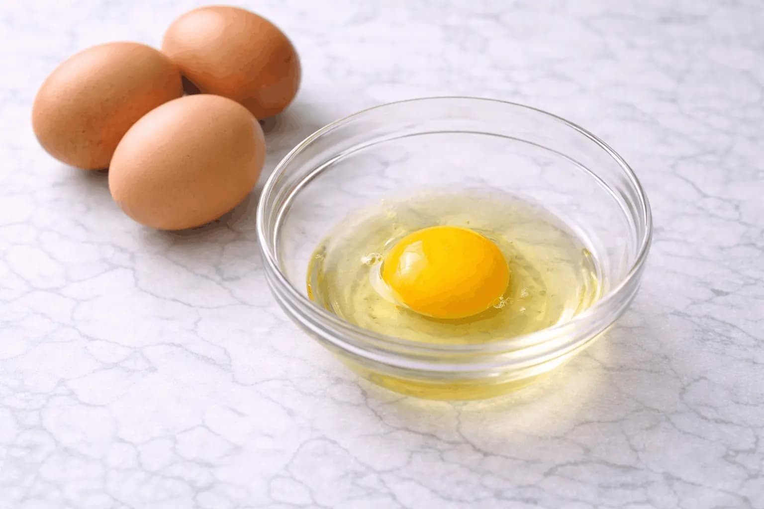 Raw egg cracked into glass bowl with whole eggs showing food safety question about eating raw eggs